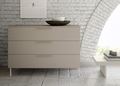 a white brick wall with a bowl on top of the dresser in front of it