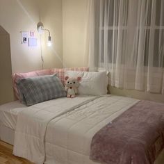 a teddy bear sitting on top of a bed in a room with white walls and curtains