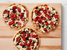 three small pizzas with tomatoes and cheese on a cutting board