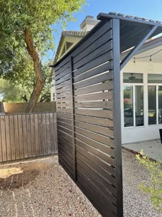 a black wooden fence in front of a house with a patio and large trees behind it