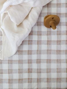 a brown teddy bear sitting on top of a white and tan checkered bed sheet