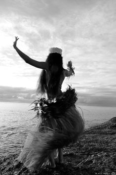 a woman is dancing on the beach with her arms in the air while wearing a hula skirt