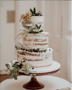 a three tiered wedding cake with greenery and berries on the top is sitting on a table