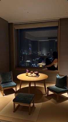 two chairs and a table in front of a large window with city lights seen through it