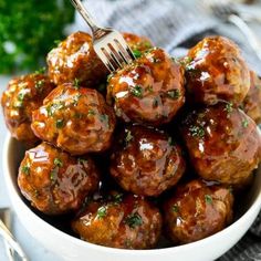 a white bowl filled with meatballs covered in sauce and garnished with parsley