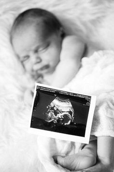 a baby laying on top of a white blanket next to a hand holding an object