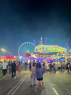 several people are standing in front of an amusement park at night with lights and rides