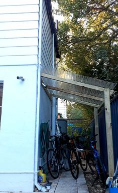 several bikes are parked under an attached pergolated area on the side of a house