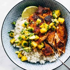 a bowl filled with rice, chicken and pineapple salsa next to a lime wedge