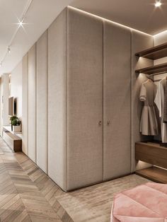 a walk in closet with clothes hanging on the wall and an ottoman next to it