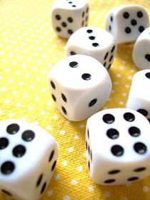 several white dices with black dots are on a yellow tablecloth and there is one in the middle