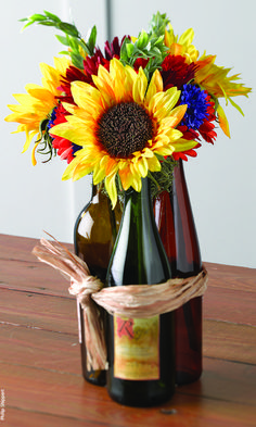 two wine bottles with sunflowers in them tied to twine on a table