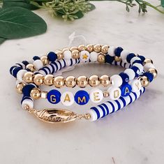 three different bracelets with gold beads and name charms on them sitting on a marble surface