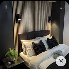 a bed with white sheets and black pillows in a room next to a wall mounted lamp