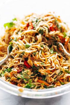 a bowl filled with noodles and vegetables on top of a white countertop next to a silver spoon