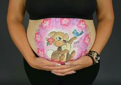 a pregnant woman is holding her belly painted with an image of a teddy bear on it