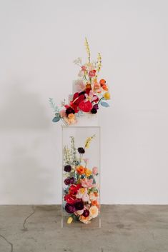 a vase filled with flowers on top of a cement floor next to a white wall