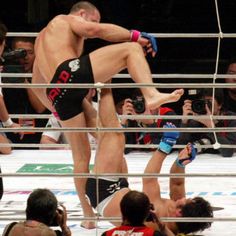 two men wrestling in an arena surrounded by people taking pictures with their cell phones and cameras