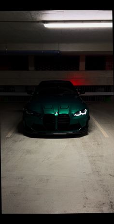 a green sports car is parked in a parking garage with its lights on at night