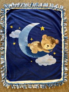 a blue blanket with a teddy bear sitting on top of the moon and stars in the sky