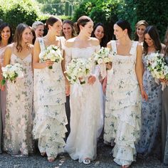 a group of women standing next to each other wearing dresses and holding bouquets in their hands