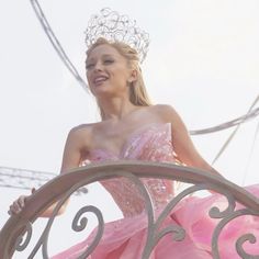 a woman in a pink dress and tiara standing on top of a metal railing