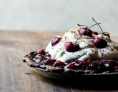 a pie topped with whipped cream and cherries on top of a wooden table in front of a wall