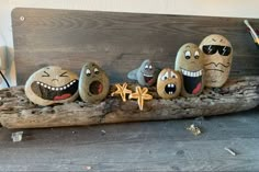 five rocks with faces painted on them sitting on a piece of driftwood next to a pencil