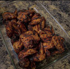 a glass dish filled with chicken wings on top of a counter