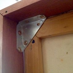 the corner of a wooden cabinet with two metal brackets on it's side and one is missing