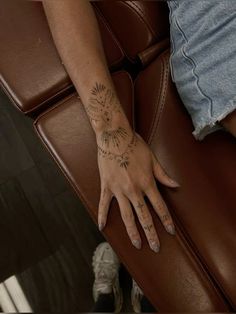 a woman's hand with tattoos on it sitting on a chair in front of a window