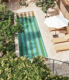 an aerial view of a pool with lounge chairs and umbrellas next to it, surrounded by greenery