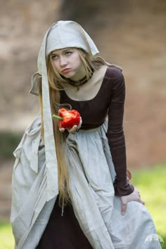 a woman dressed as a nun holding a red pepper in her hand and looking at the camera