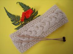 a knitted headband next to a red flower on a yellow background with green leaves