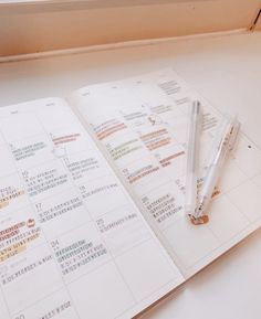 an open planner and pen sitting on top of a white table next to a window