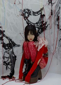 a woman sitting on the ground in front of a wall with many strings attached to it