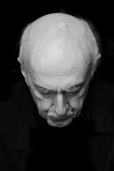 an older man with white hair and beards looking down at his cell phone while wearing a black shirt