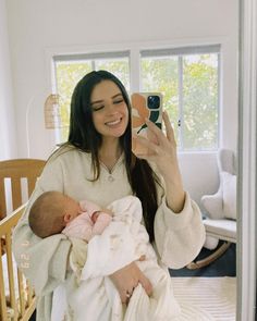 a woman holding a baby in her arms and taking a selfie with the phone