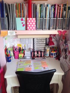 a white desk topped with lots of books and office supplies next to a shelf filled with binders