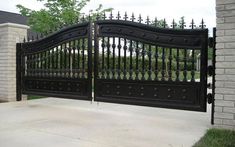 an iron gate in front of a brick wall and stone pillars on the side of a driveway