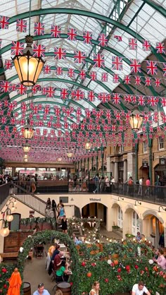 an indoor shopping mall filled with lots of flowers and flags hanging from the ceiling above