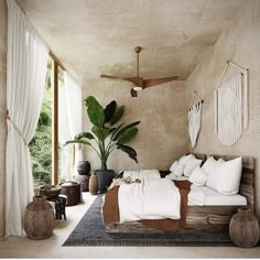 a bed with white sheets and pillows in a room next to a plant on the floor