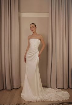 a woman standing in front of curtains wearing a white dress