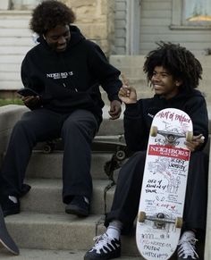 two people sitting on steps with skateboards in their hands and one person pointing at the camera