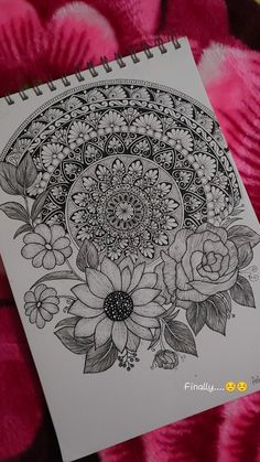 a spiral notebook with flowers and leaves drawn on the cover, sitting on a pink blanket