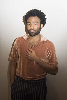 a man standing in front of a white wall with his hand on his chest and looking at the camera