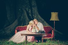 a bride and groom sitting on a red couch in front of a tree at night