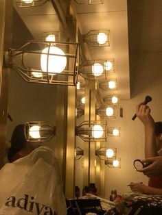 a woman is brushing her teeth in front of a mirror with lights on the ceiling