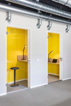 two open doors in an office with yellow walls and metal piping on the ceiling