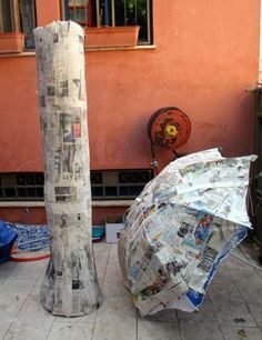 an open umbrella sitting on the ground next to a pole with newspaper covering it's sides